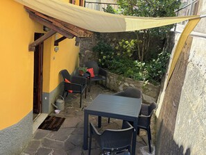 Une terrasse extérieure avec un sol en pierre, une table, des chaises et un mur jaune.