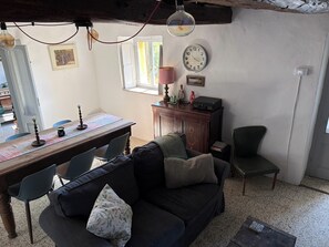 Ein gemütlicher Wohnbereich mit einem dunkelgrauen Sofa, einem Holzesstisch mit Stühlen, einer Uhr und einer kleinen Kommode mit Dekoration.