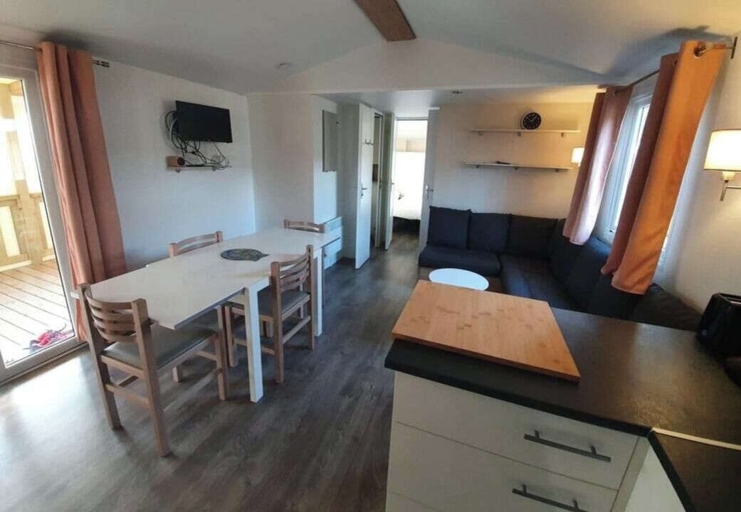 A compact living space with a dining area, a kitchenette, a sofa, and a television mounted on the wall.