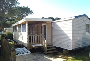 A mobile home with a porch, a small table, and a staircase leading to the entrance. - Vrbo Property (Quiberon)