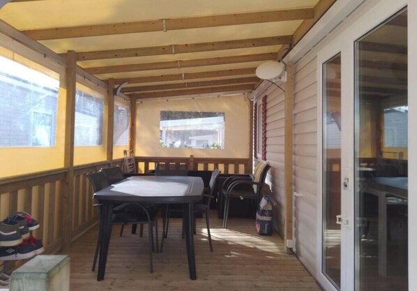 A covered patio with a table and chairs, wooden beams, and a sliding glass door. - Vrbo Property (Quiberon)