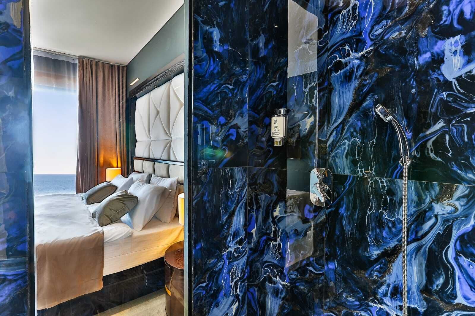 A hotel room with a bed, a view of the sea, and a bathroom with a marble wall.