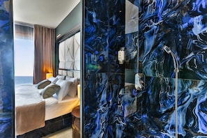 Habitación de hotel con cama, vista al mar y baño con pared de mármol.