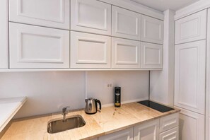 Una cocina con gabinetes blancos, un lavamanos de acero inoxidable, una tetera y una lata de café.