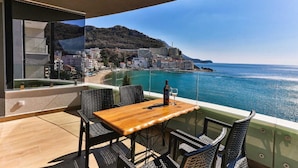 Un balcón con mesa y sillas de madera, con vistas a un pueblo costero y al mar.