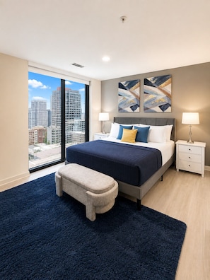 Een moderne slaapkamer met een groot bed, een bankje, een nachtkastje en uitzicht op de stad door een groot raam.