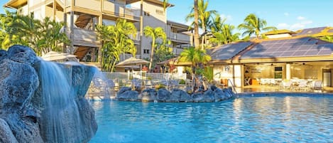 A hotel with a pool, palm trees, and a waterfall.