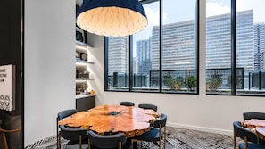 A modern meeting room with a large wooden table, black chairs, and a city view through large windows. - Urban City Luxe | Luxury 2BR | Year-Round Pool | Balcony Views| Walk Everywhere (Atlanta)