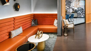 A modern lounge area with a curved orange sofa, a round marble coffee table, and a seating area with blue chairs and a wooden sideboard. - Urban City Luxe | Luxury 2BR | Year-Round Pool | Balcony Views| Walk Everywhere (Atlanta)