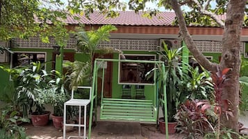 A green outdoor area with a swing, potted plants, and a building with a tiled roof.