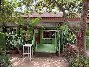 A green outdoor area with a swing, potted plants, and a building with a tiled roof. - Lovely Bedroom bungalow with AC in Siem Reap (Siem Reap)