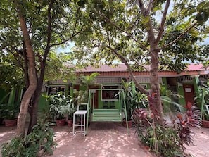 Un patio con un banco verde, plantas en macetas y suelo de baldosas.