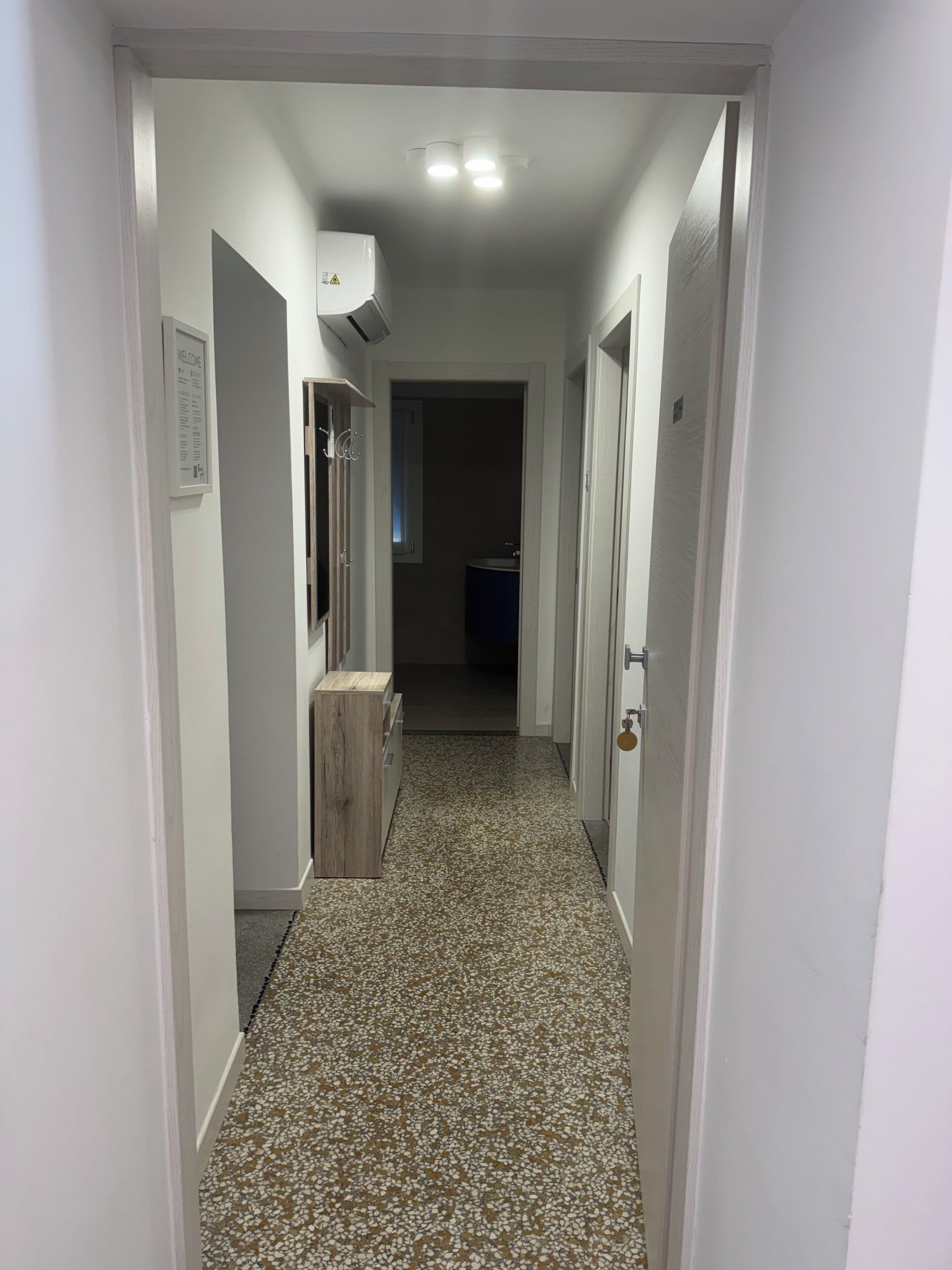 A hallway with white walls, a tiled floor, and a door at the end leading to a dark room.