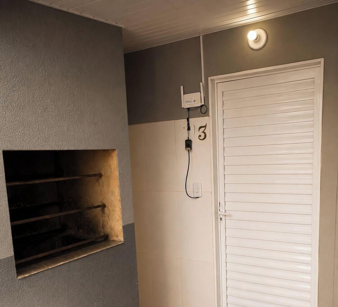 Una stanza con una porta bianca, una piccola finestra e uno scaffale metallico, oltre a una presa elettrica fissata al muro con un cavo.