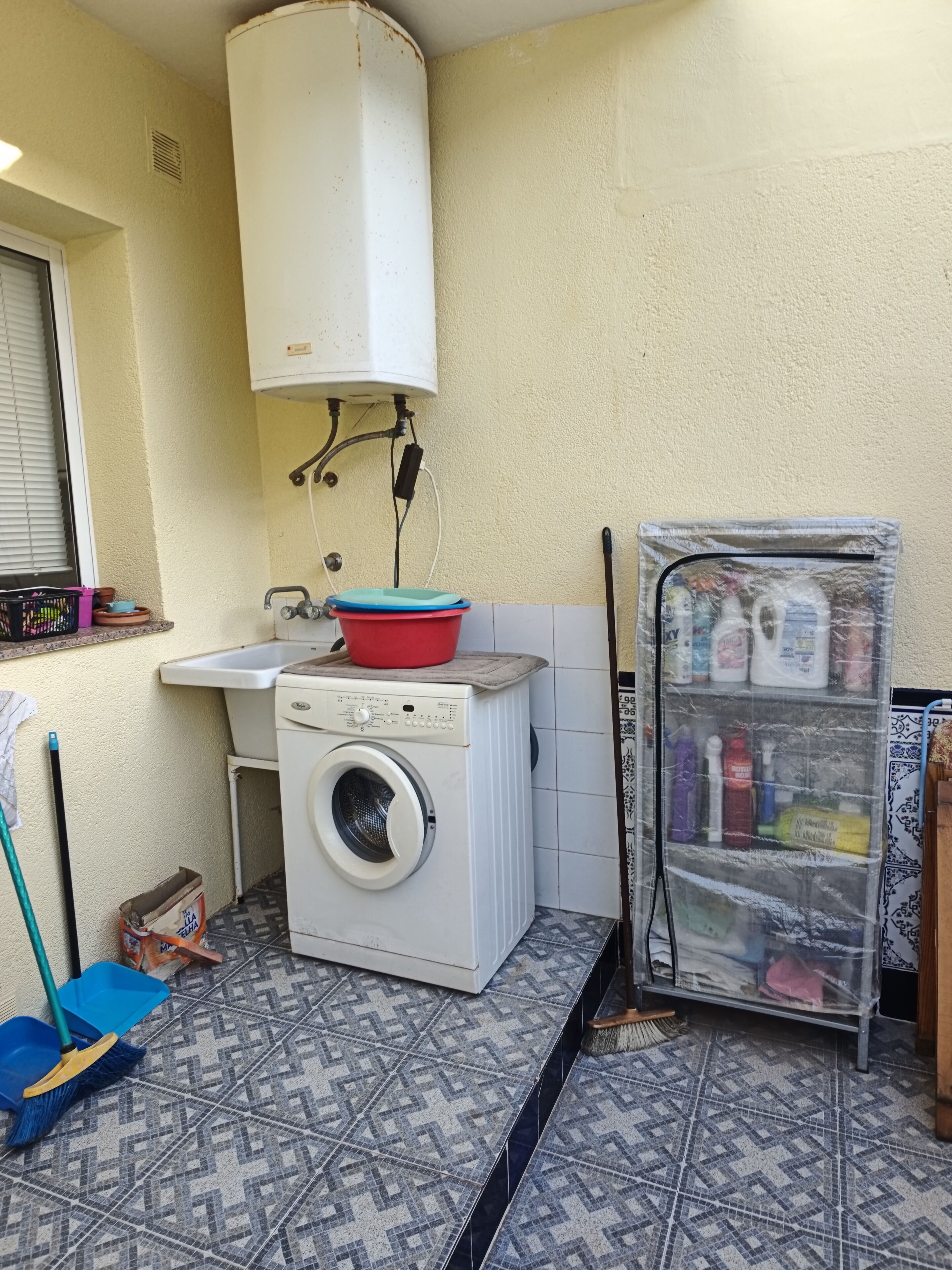 Une petite buanderie équipée d’un lave-linge, d’un évier et d’un chauffe-eau.