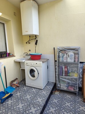 Une petite buanderie équipée d’un lave-linge, d’un évier et d’un chauffe-eau.