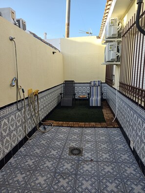 A small, enclosed outdoor area with a patterned floor, a small seating area, and a water spigot. - CASA RAQUELITA Cozy Townhouse (Los Alcázares)