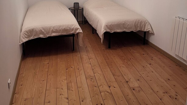 A room with two single beds, a small table, and a ceiling light fixture.