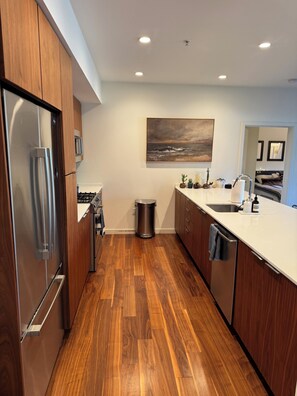 Een moderne keuken met houten kastjes, roestvrijstalen apparatuur en een wit aanrecht.