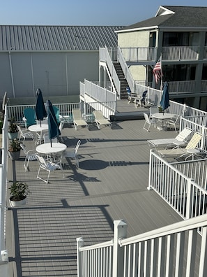 Eine Terrasse mit Sitzgelegenheiten im Freien, darunter Tische und Stühle, und eine Treppe, die zu einer oberen Ebene führt.