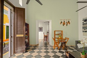 Ein Zimmer mit Schachbrettfußboden, einem Esstisch mit Stühlen, einem Bücherregal und einer zur Außenseite führenden Tür.