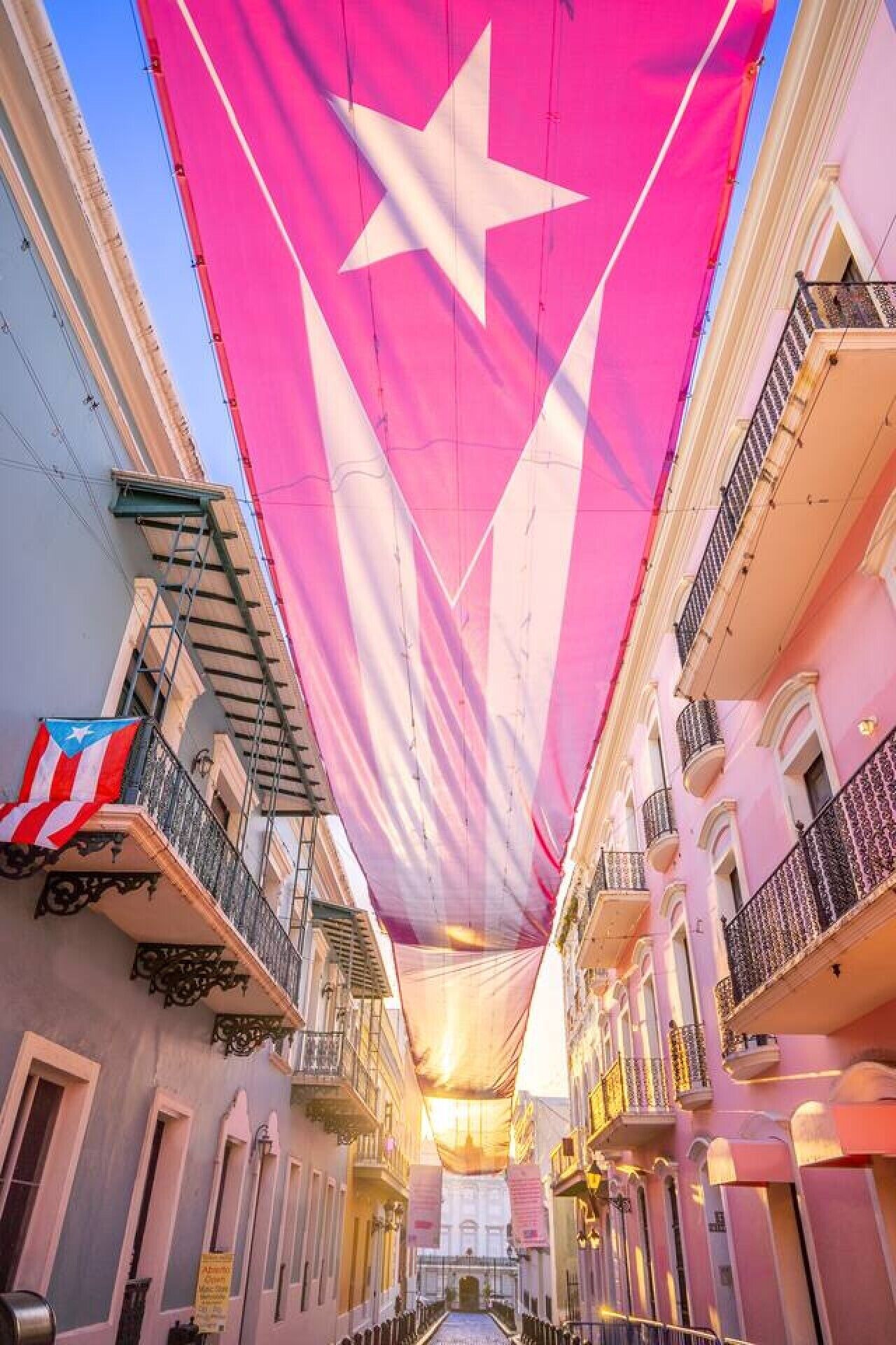 Rua com edifícios de ambos os lados, uma grande bandeira e varandas.