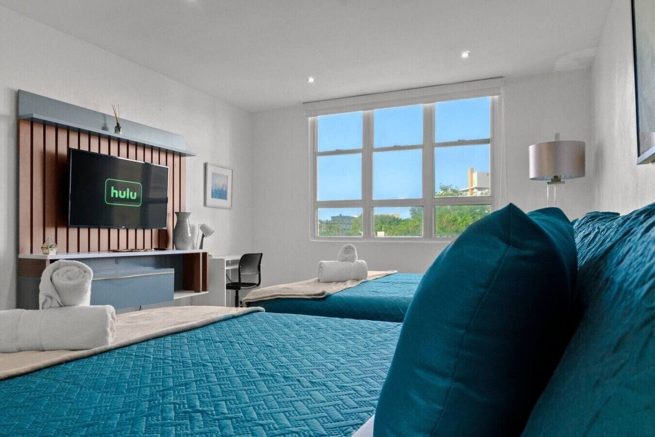 A hotel room with two beds, a desk, a television, and a large window.