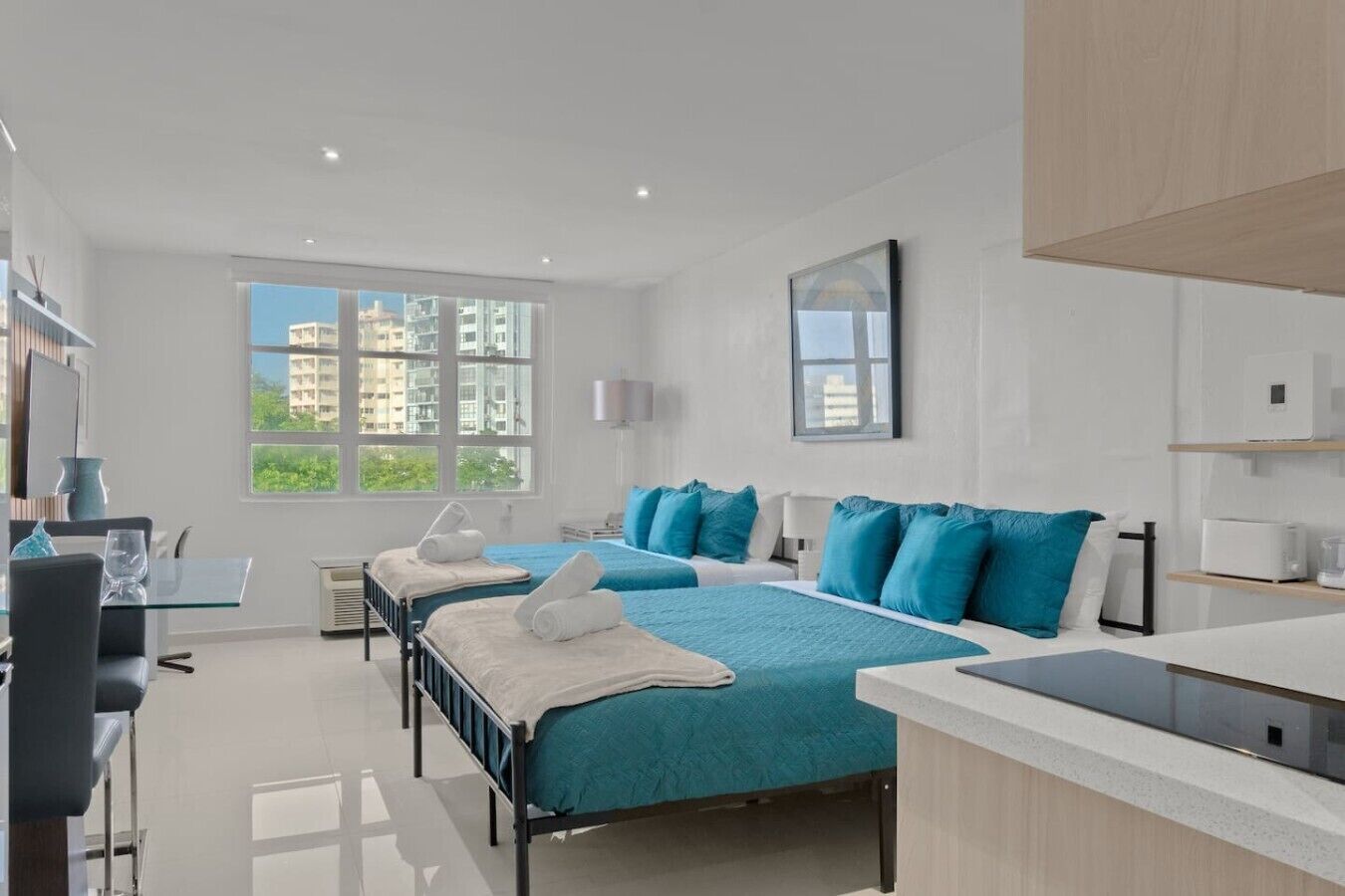 A modern hotel room with two beds, a dining area, and a view of buildings.