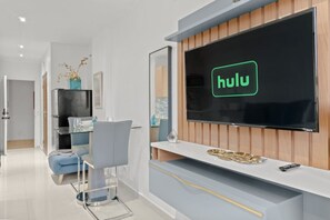 A modern living room with a large flat-screen TV mounted on a wooden wall, a glass coffee table, a blue sofa, and a minimalist decor style. - T-Mobile District San Juan Next to Beach (San Juan)