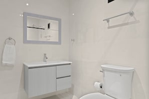 Un baño moderno con lavabo, espejo y retrete blancos.