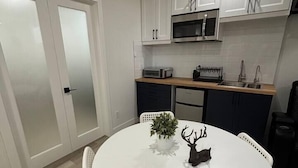 A compact kitchen with white cabinets, a microwave, and a dining area with a round table and chairs.