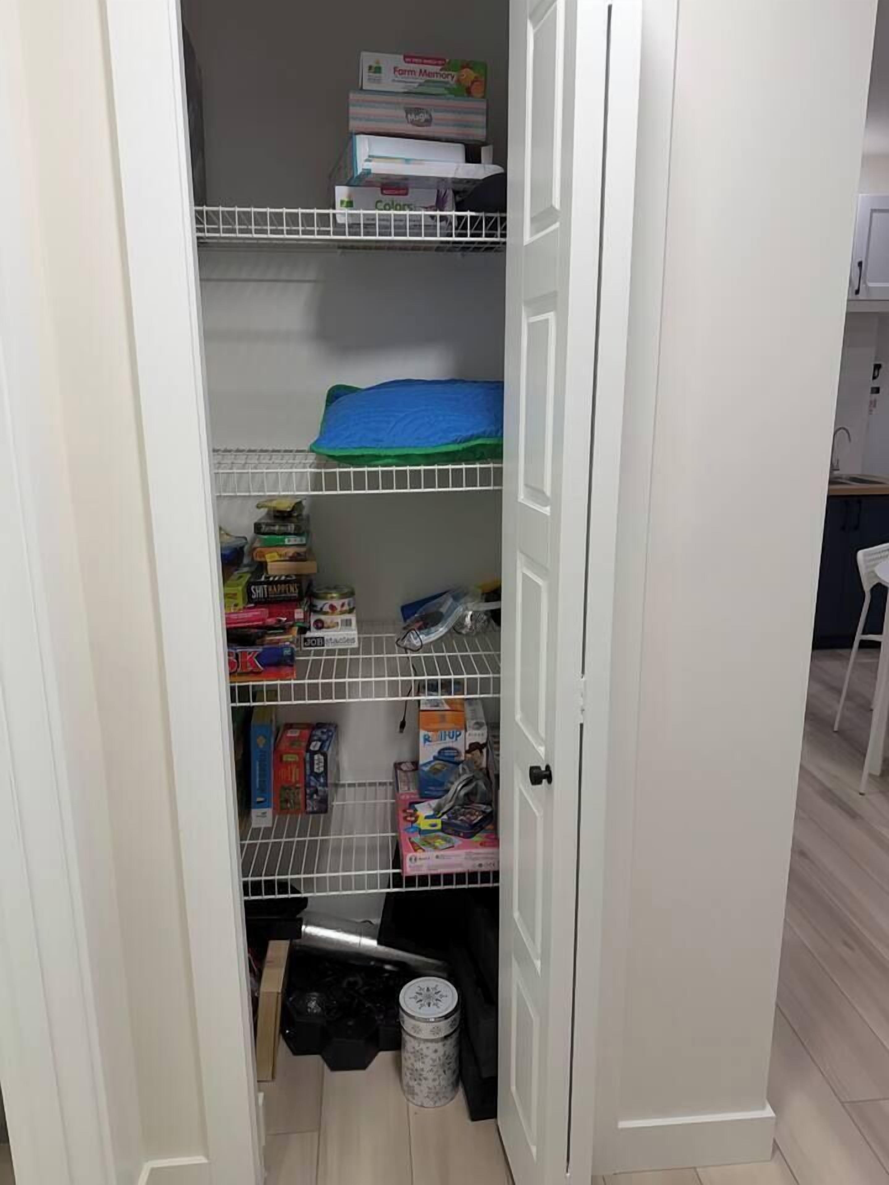 A narrow walk-in closet with shelves containing various items, including boxes and a trash bin.