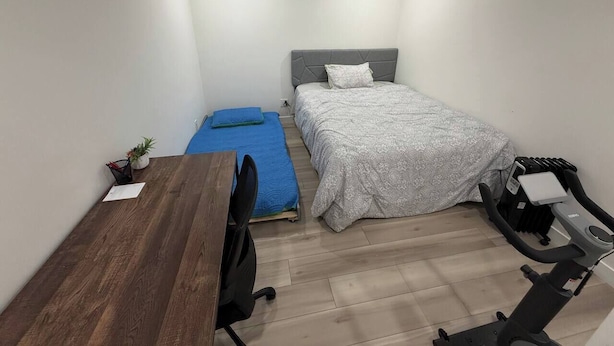 A compact room with a bed, a desk, a chair, and a treadmill.