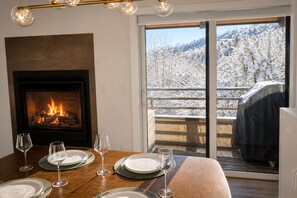 Un comedor con chimenea, una mesa lista para cuatro personas y vistas a un paisaje nevado a través de un ventanal corredera.