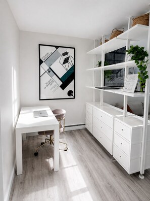 Una habitación moderna y minimalista con un escritorio blanco, una silla, estantería blanca y un cuadro en la pared.