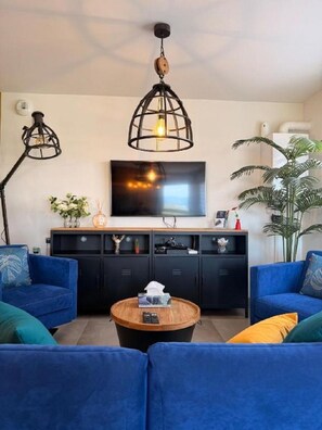 Ein Wohnzimmer mit einer Sofagarnitur, einem Couchtisch, einem an der Wand befestigten Fernseher und einer großen Pflanze.