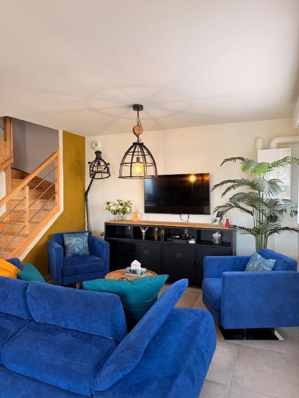 Ein Wohnzimmer mit Treppe, Flachbildfernseher und einer großen Pflanze.