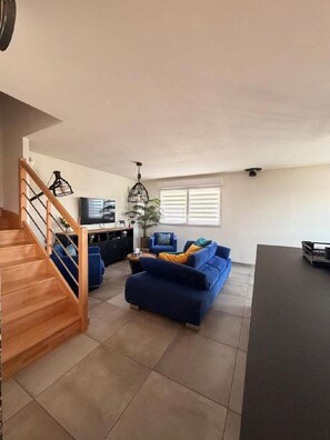 Amplia sala de estar con una escalera de madera, un sofá azul, una mesa de comedor y una televisión.