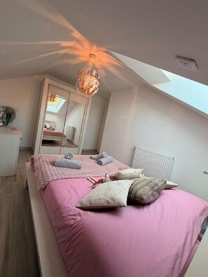 Een slaapkamer met een schuine kap, dakraam, een bed met roze beddengoed en een witte radiator.