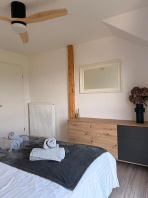 Een slaapkamer met een bed, een houten dressoir, een radiator, een plafondventilator en een ingelijste foto aan de muur.