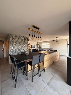 Una cocina moderna con una isla central, una mesa de comedor con sillas e iluminación colgante.