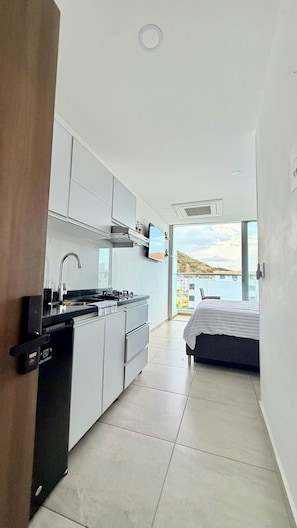 A modern kitchen with a built-in dishwasher, a sink, and a stove. There is a bed with a white bedspread in the adjacent room. - Edificio Sky Tower (Gaira)