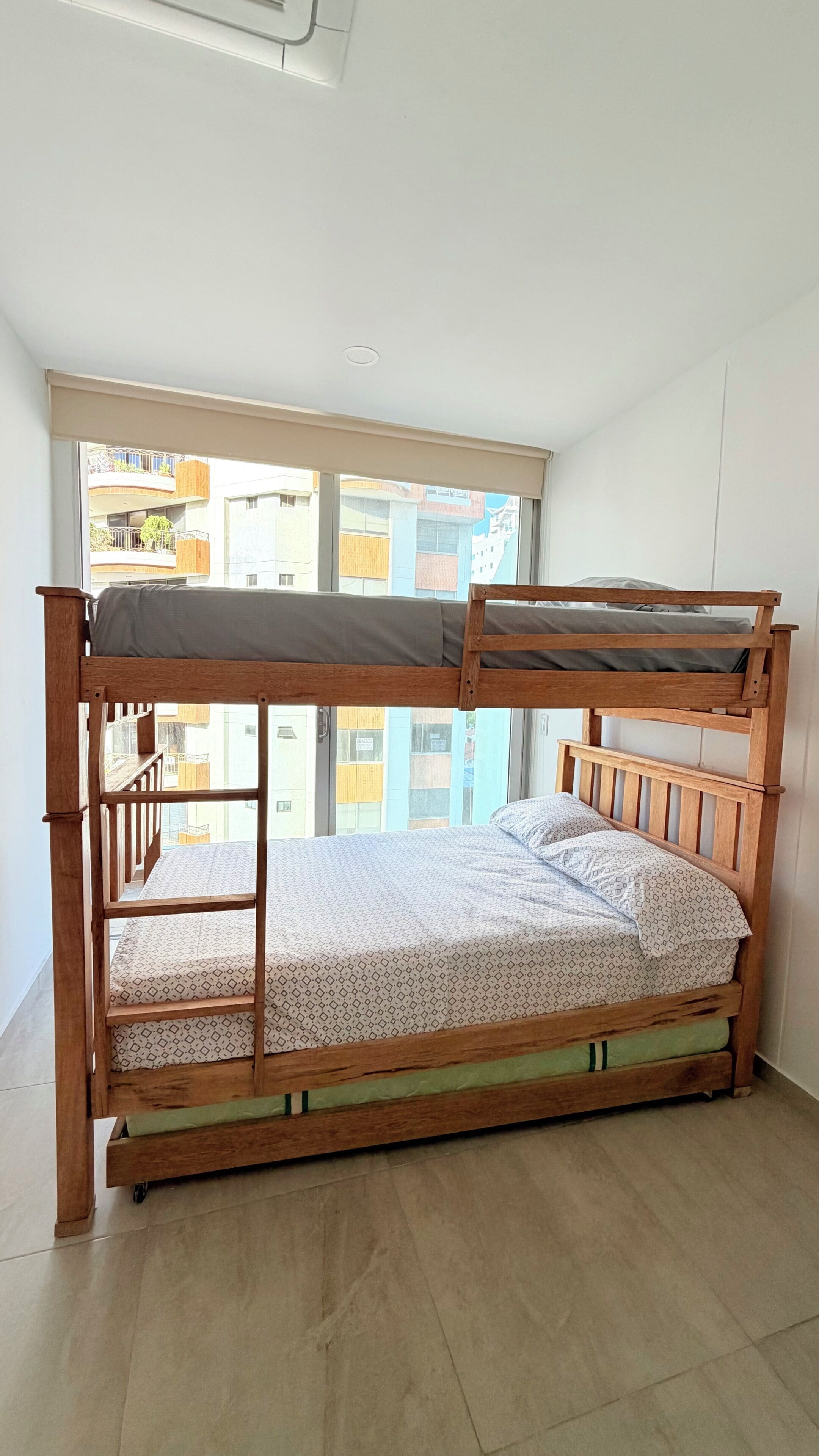 A bunk bed with a view of buildings through a window.