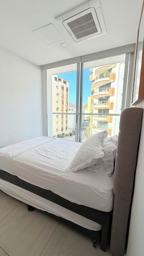 A bedroom with a bed, a window, and a view of buildings outside.