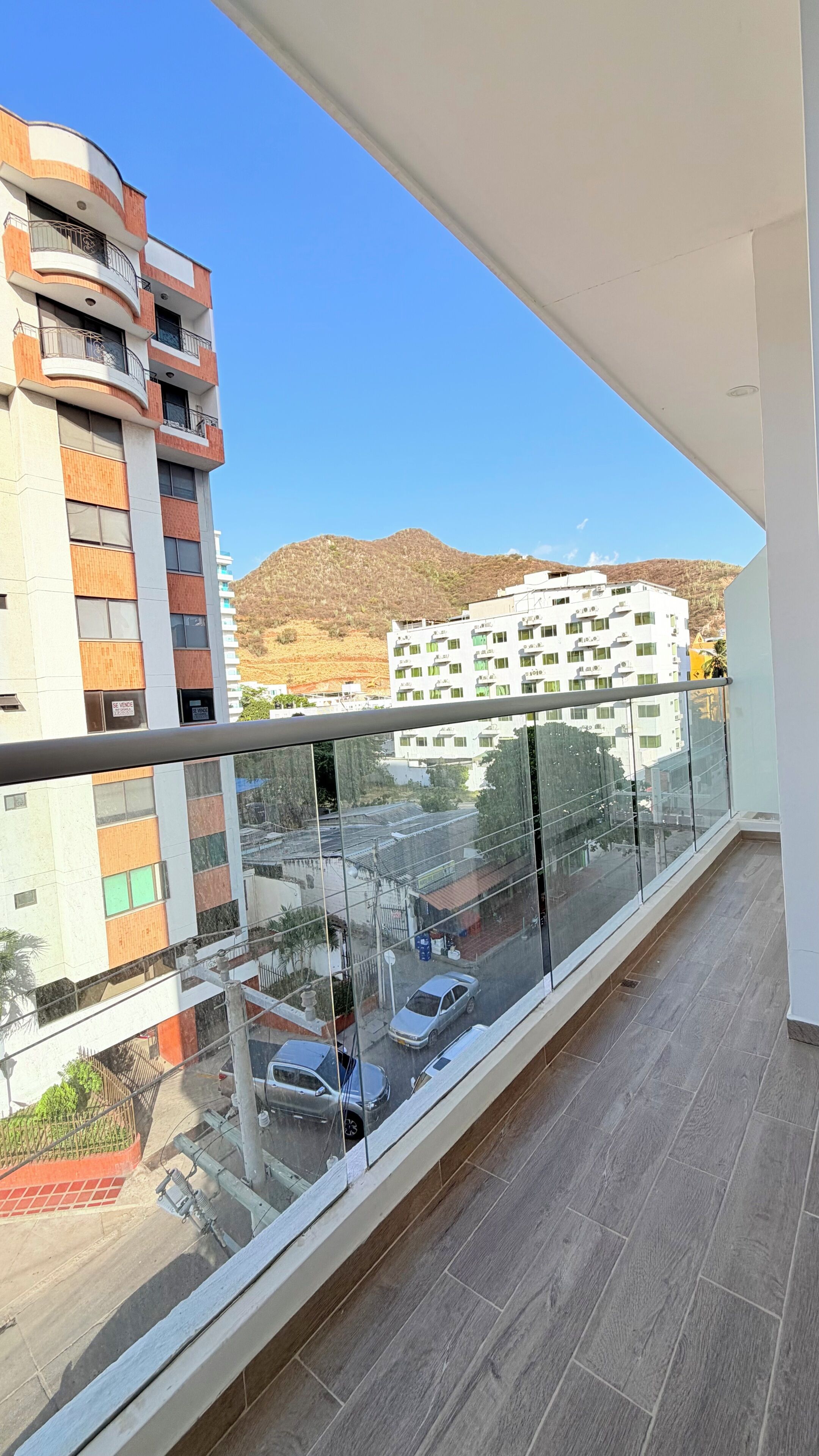 A balcony with a view of a street, buildings, and a hilly landscape.