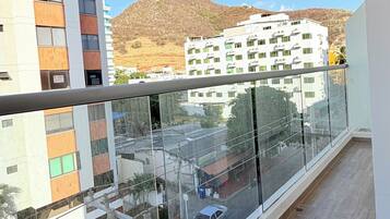A balcony with a view of a street, buildings, and a hilly landscape.