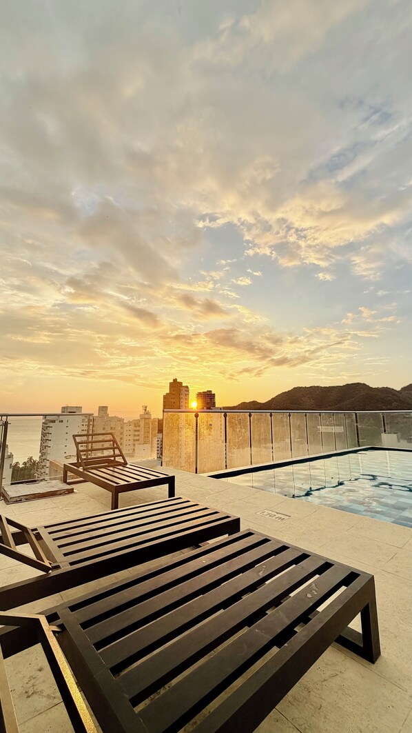 A rooftop pool area with lounge chairs and a view of the sunset over a cityscape. - Edificio Sky Tower (Gaira)