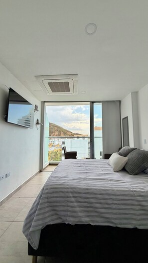 A modern bedroom with a large bed, a flat-screen TV, and a view of a body of water. - Edificio Sky Tower (Gaira)