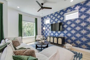 A modern living room with a sofa, a coffee table, a TV mounted on the wall, and a patterned wallpaper. - Spa Soaker Tub & Patio Near Downtown Houston & University of Houston (Houston)