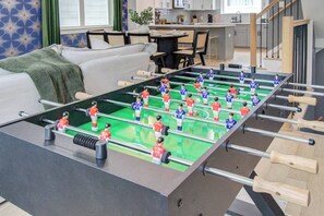 A foosball table in a modern living room with a sofa and a dining area in the background. - Spa Soaker Tub & Patio Near Downtown Houston & University of Houston (Houston)